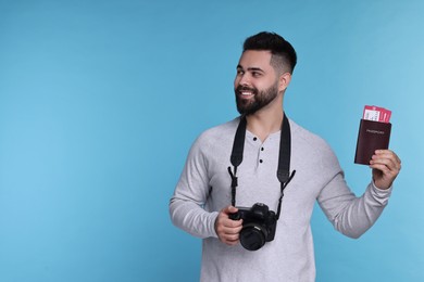 Photo of Happy man with passport, tickets and camera on light blue background. Space for text