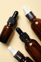 Many bottles with face serums on beige background, flat lay