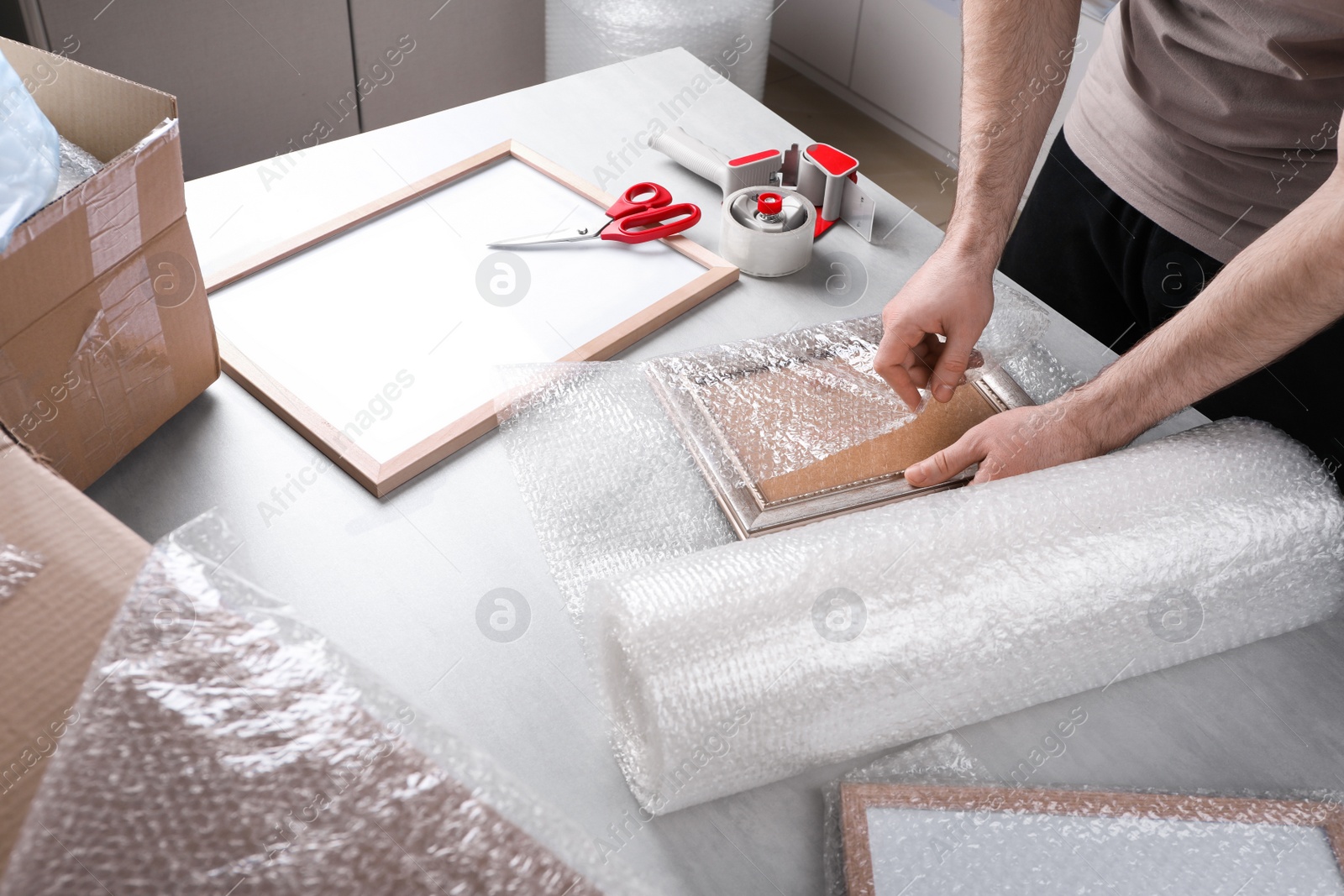 Photo of Man covering photo frame with bubble wrap at light grey table, closeup