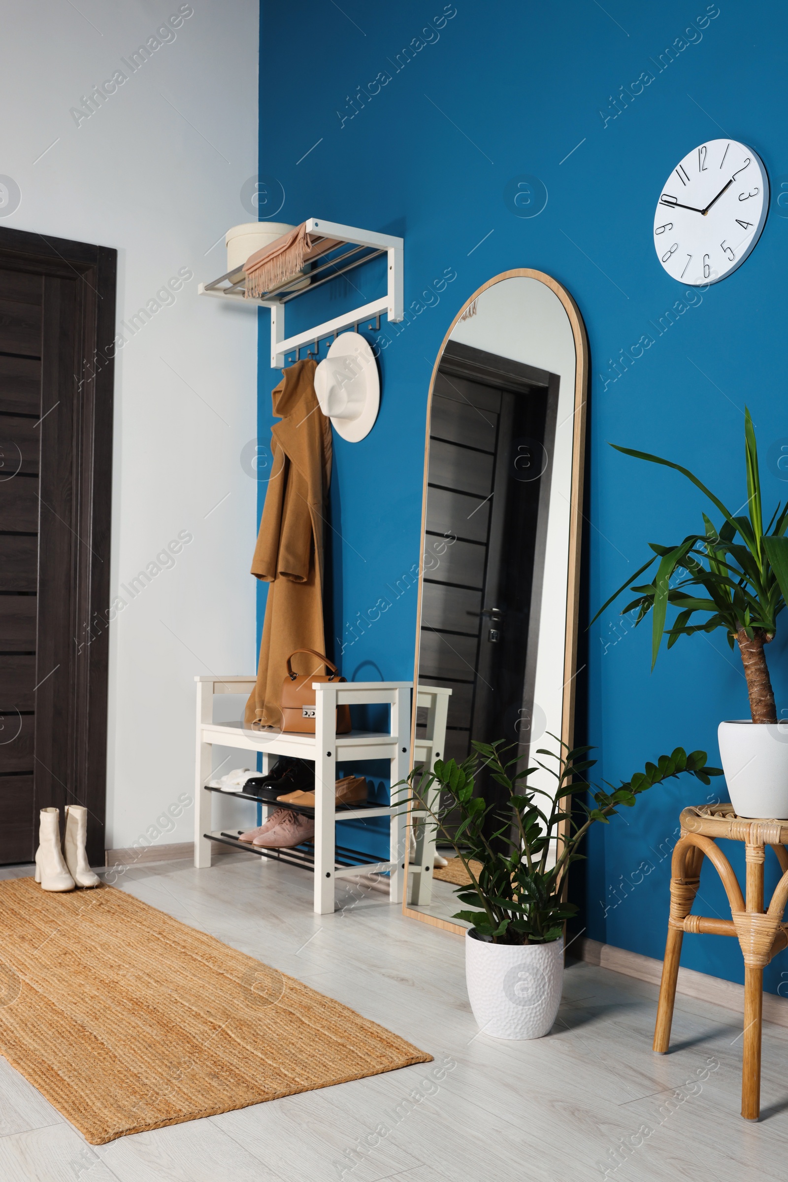 Photo of Stylish hallway with shoe storage bench and mirror near blue wall. Interior design