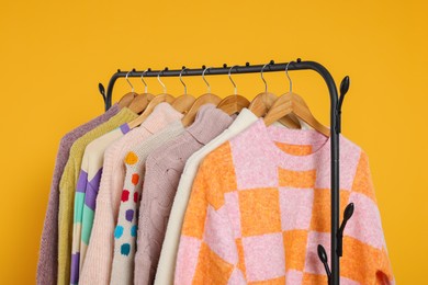 Photo of Rack with stylish women's sweaters on wooden hangers against orange background