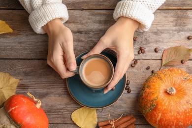 Photo of Woman holding cup with pumpkin spice latte on wooden background, top view