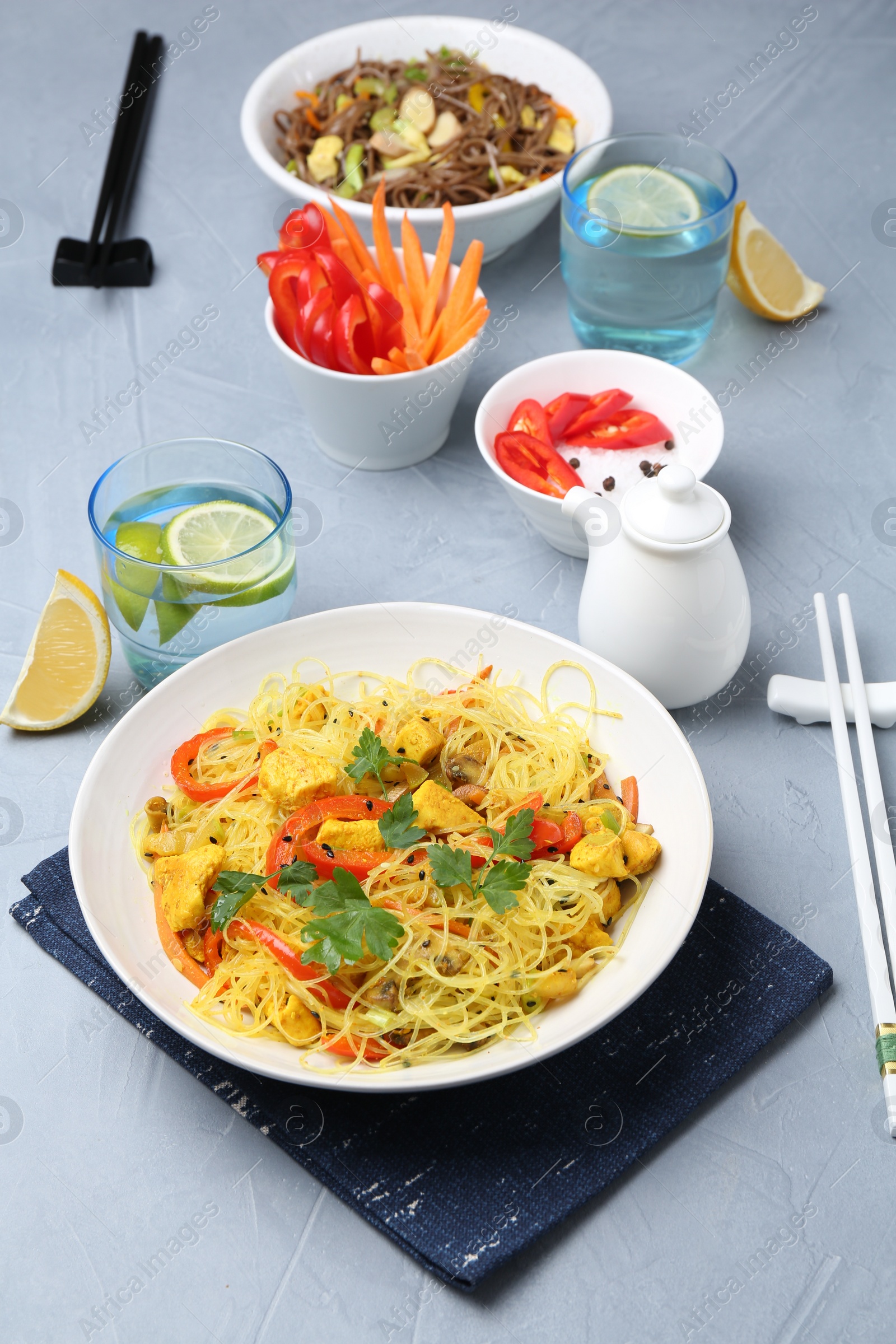 Photo of Stir-fry. Delicious cooked noodles with chicken and vegetables in bowls served on gray textured table