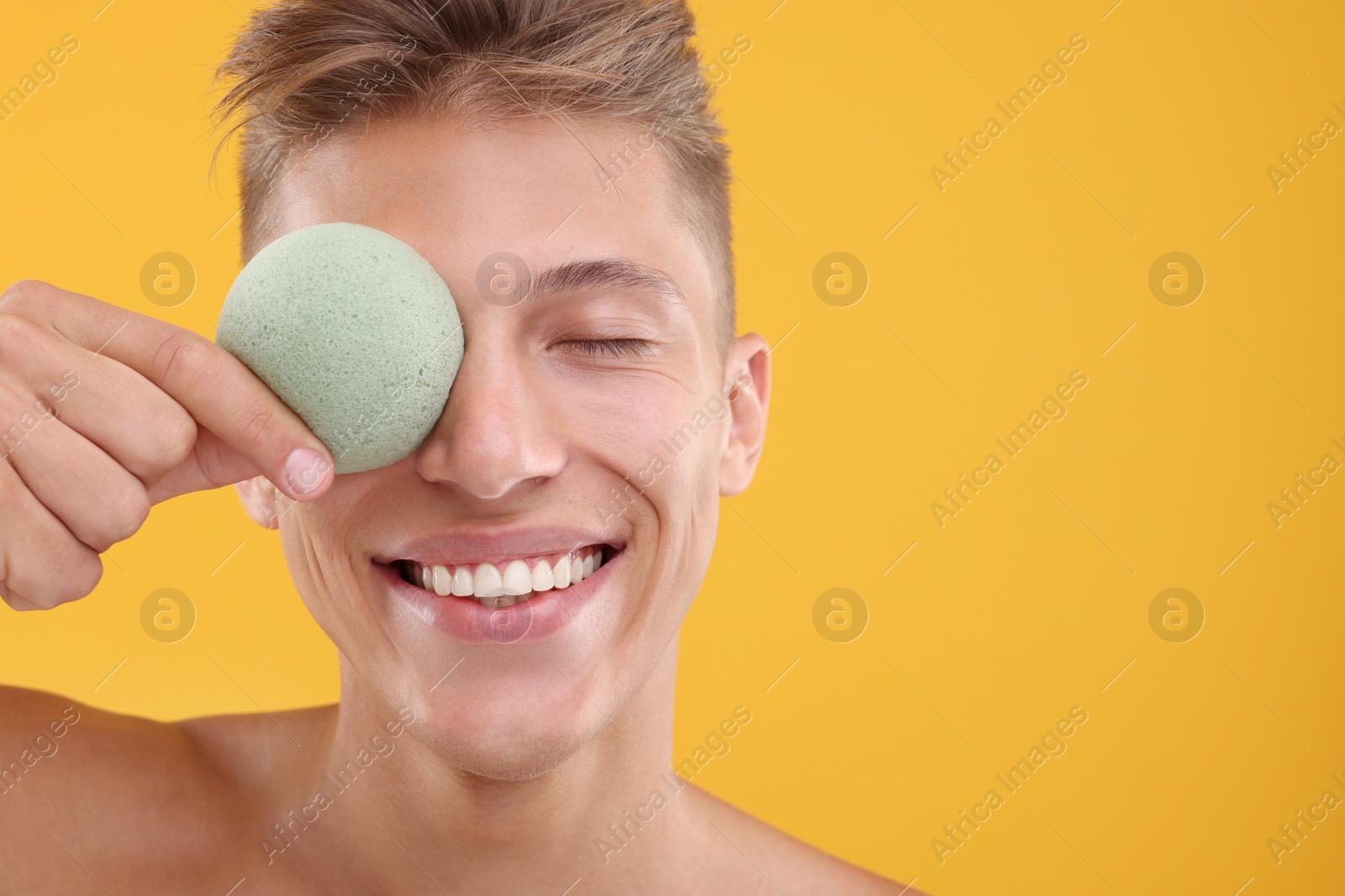 Photo of Happy young man holding face sponge on orange background. Space for text