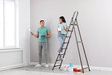 Photo of Young couple painting wall with roller and brush indoors