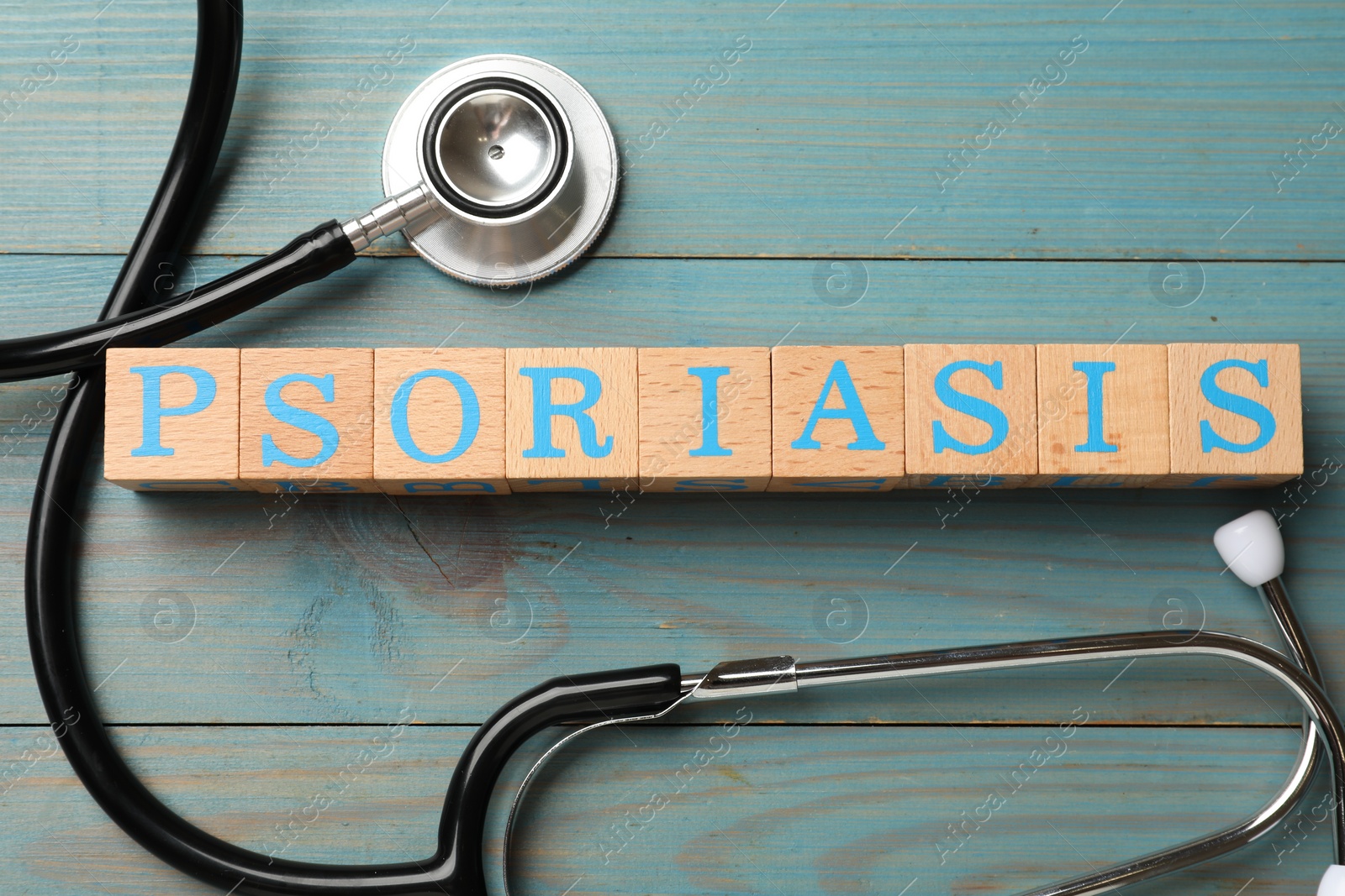 Photo of Word Psoriasis made of cubes with letters and stethoscope on light blue wooden table, flat lay