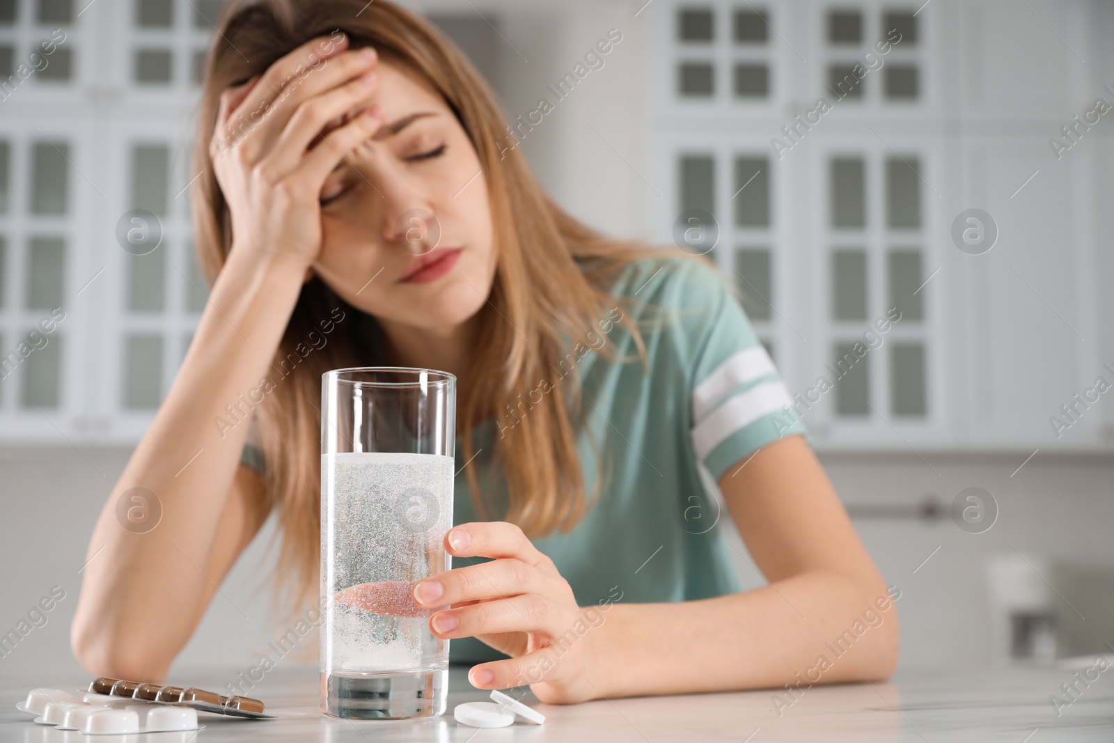 Photo of Woman taking medicine for hangover in kitchen, focus on hand with glass