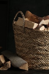 Photo of Wicker basket with cut firewood on table against dark background, closeup