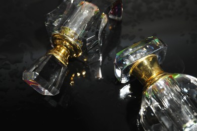 Glass perfume bottles on wet black table, closeup