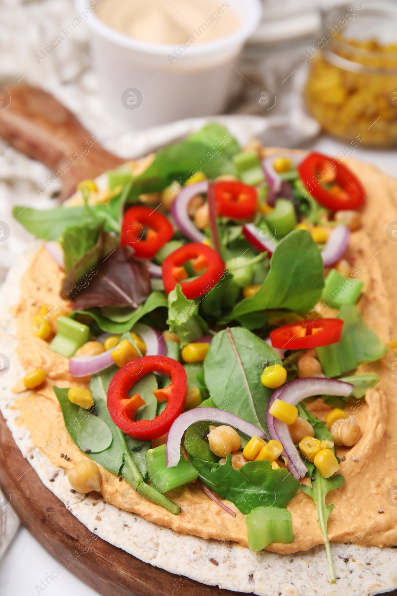 Photo of Tortilla with hummus and vegetables on table, closeup