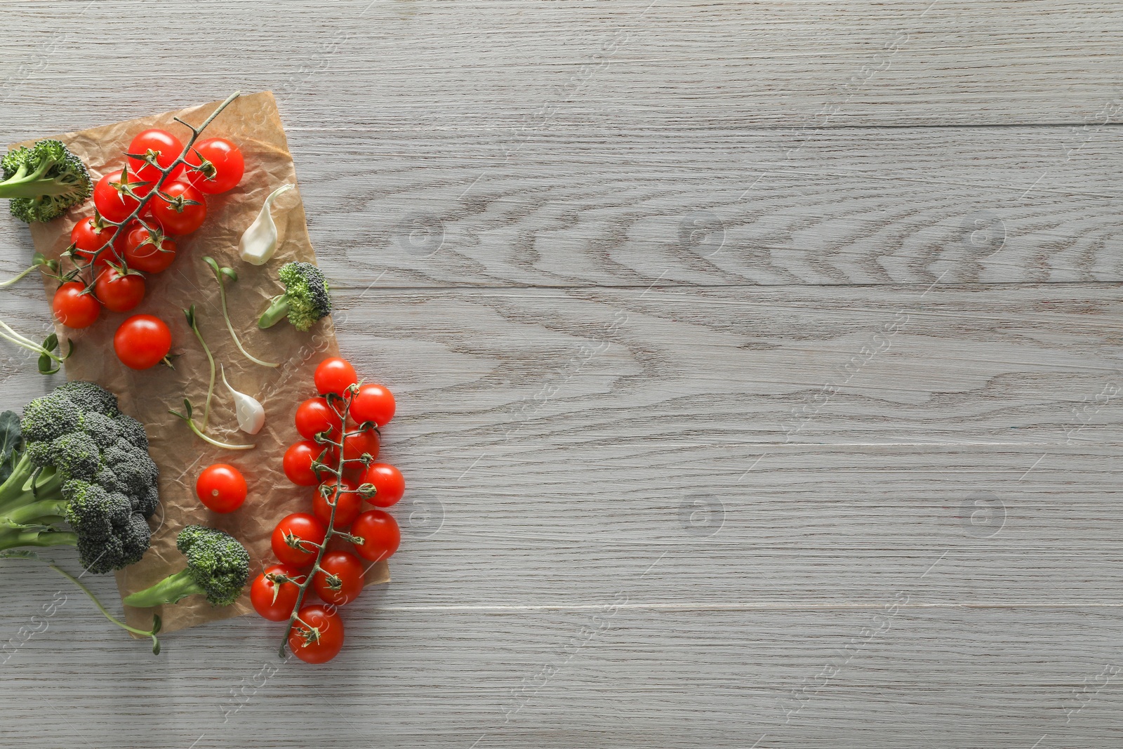 Photo of Food photography. Fresh cherry tomatoes, broccoli, garlic and microgreen on wooden table, flat lay with space for text