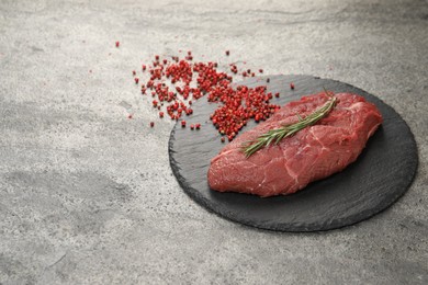 Photo of Piece of raw beef meat, rosemary and red peppercorns on grey table, space for text