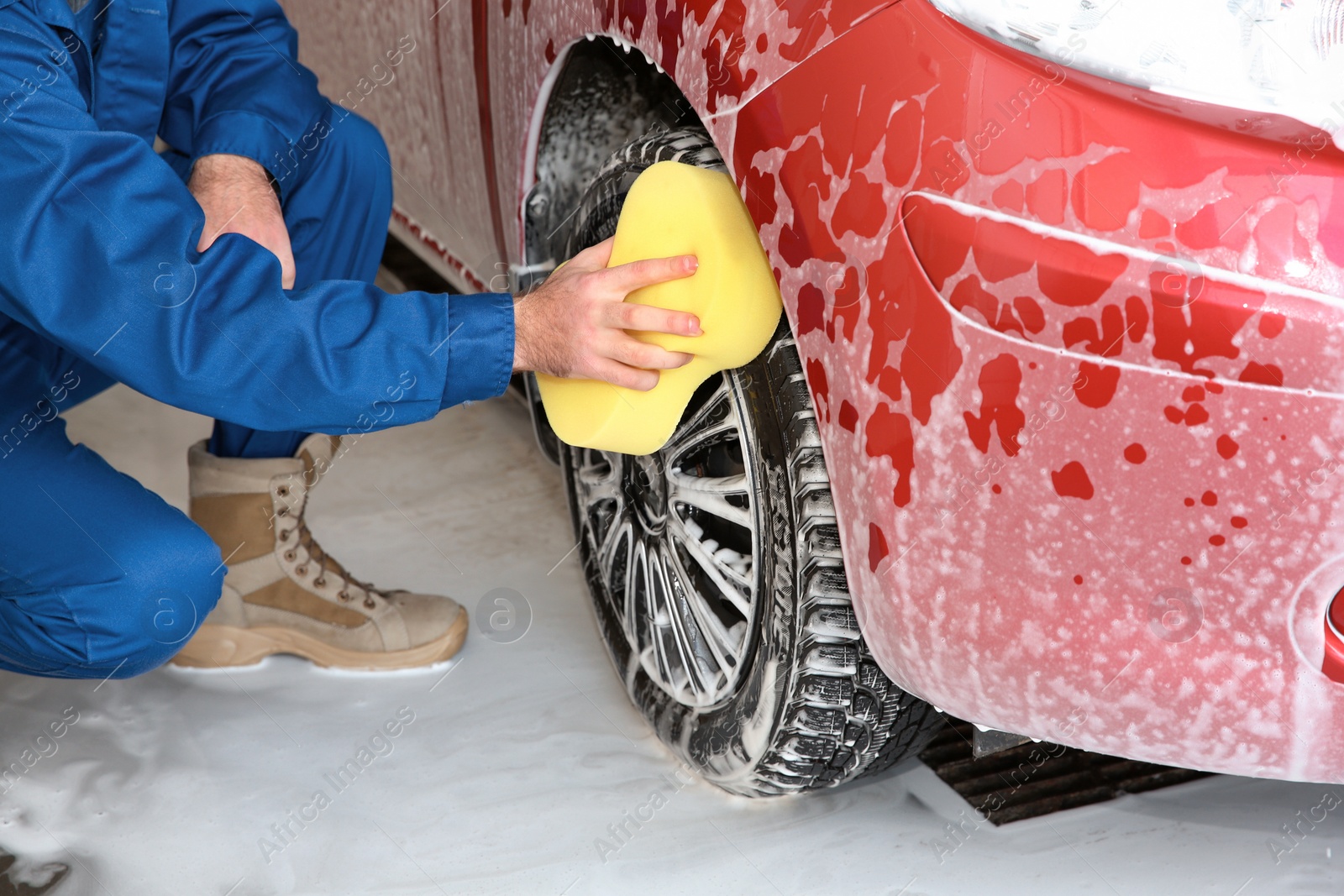 Photo of Young worker cleaning automobile wheel at car wash, closeup