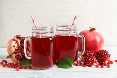 Photo of Mason jars of pomegranate juice and fresh fruits on wooden table