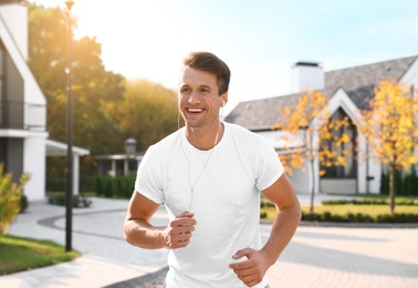 Young man with earphones running outdoors on sunny morning. Healthy lifestyle