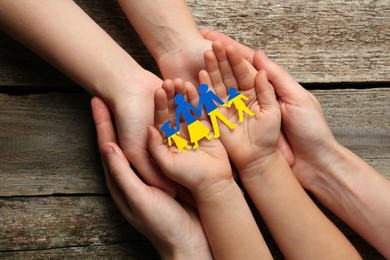 Parents and child holding paper family cutout in colors of Ukrainian flag at wooden table, top view