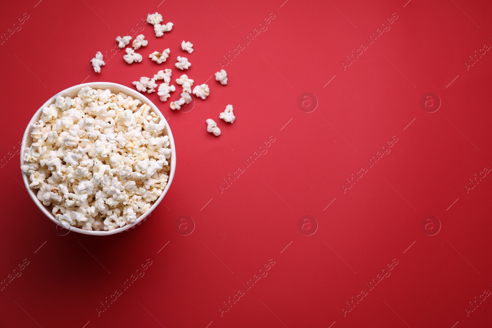 Photo of Paper bucket with delicious popcorn on red background, flat lay. Space for text
