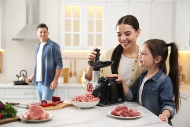 Photo of Happy family making dinner together in kitchen, mother and daughter using modern meat grinder