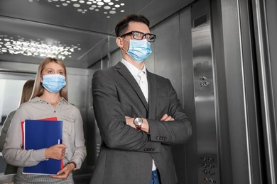 Coworkers with face masks in elevator. Protective measure