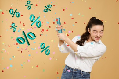 Image of Discount offer. Happy young woman blowing up party popper on dark beige background. Confetti and percent signs in air