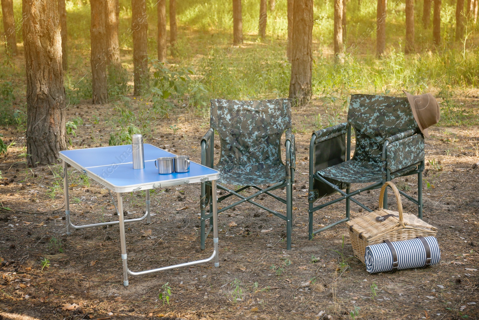 Photo of Camouflage chairs, picnic basket and table in forest on sunny day