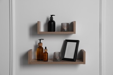 Photo of Wooden shelves with toiletries and decor on white wall. Interior design