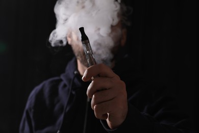 Photo of Man using electronic cigarette against black background, focus on hand