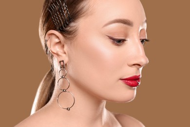 Photo of Young woman with lip and ear piercings on light brown background, closeup