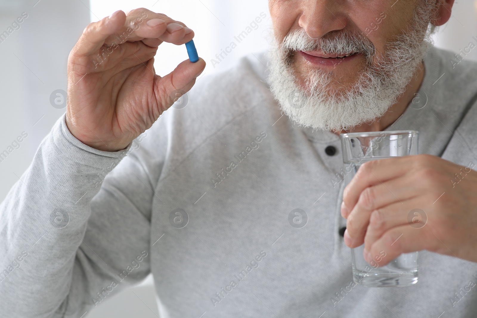 Photo of Senior man with glass of water and pill on blurred background, closeup