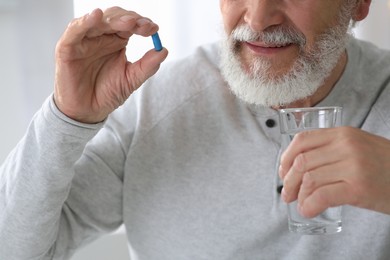 Senior man with glass of water and pill on blurred background, closeup