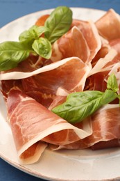 Photo of Slices of tasty cured ham and basil on plate, closeup