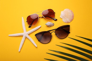 Stylish sunglasses, starfish and seashells on yellow background, flat lay