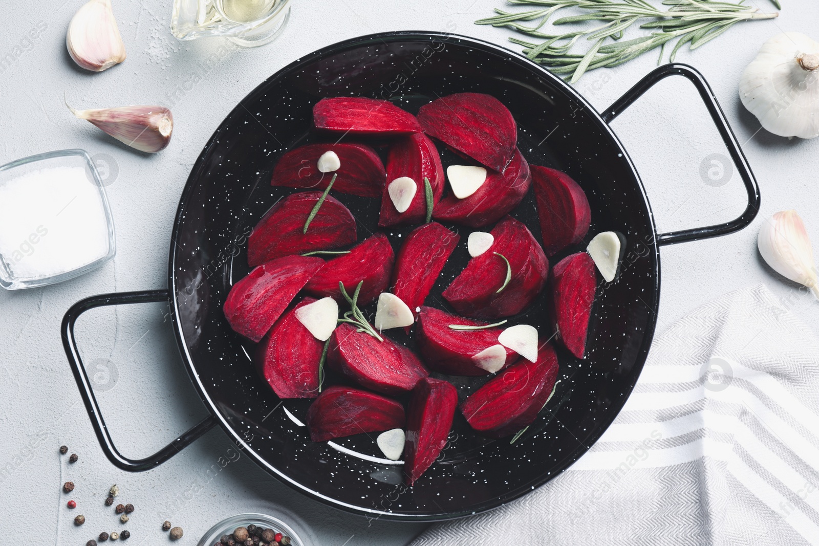 Photo of Slices of raw beetroot with garlic in wok pan on white table, flat lay