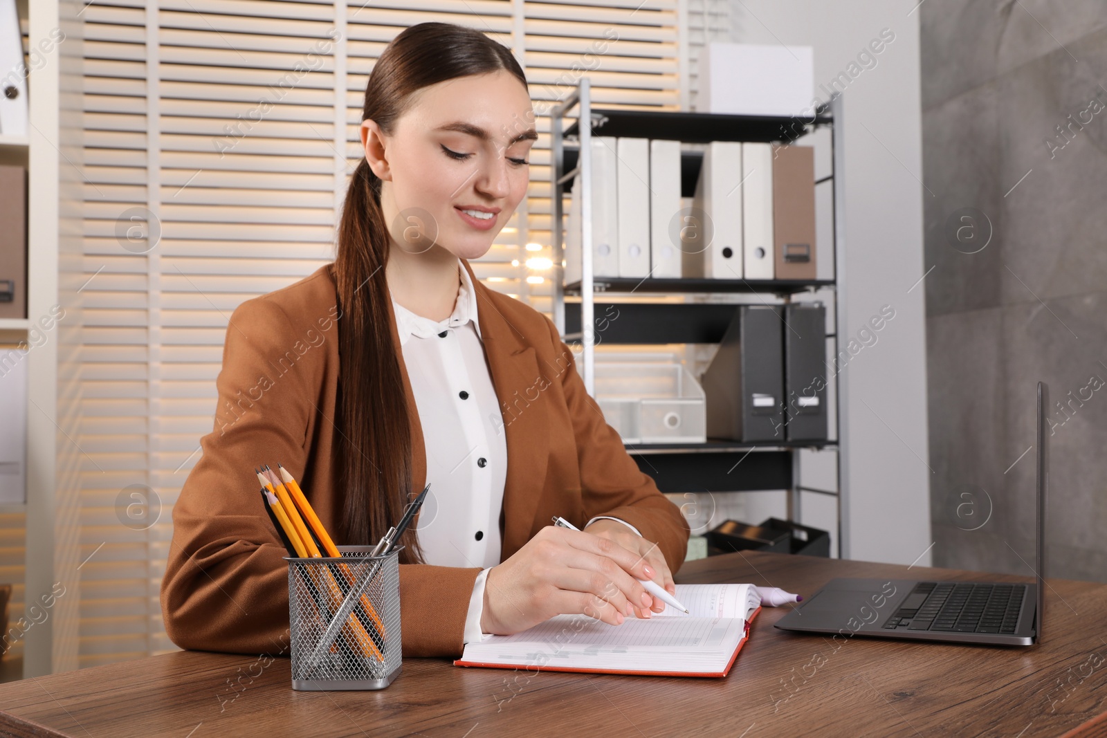 Photo of Happy woman taking notes at wooden table in office, space for text