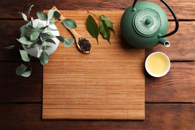 Photo of Flat lay composition with bamboo mat, dry tea leaves and teapot on wooden table, space for text