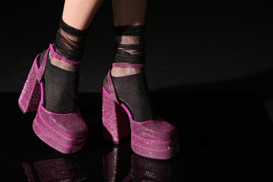 Woman wearing pink high heeled shoes with platform and square toes on black background, closeup. Space for text