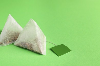 Photo of New tea bags with tabs on green background, closeup. Space for text