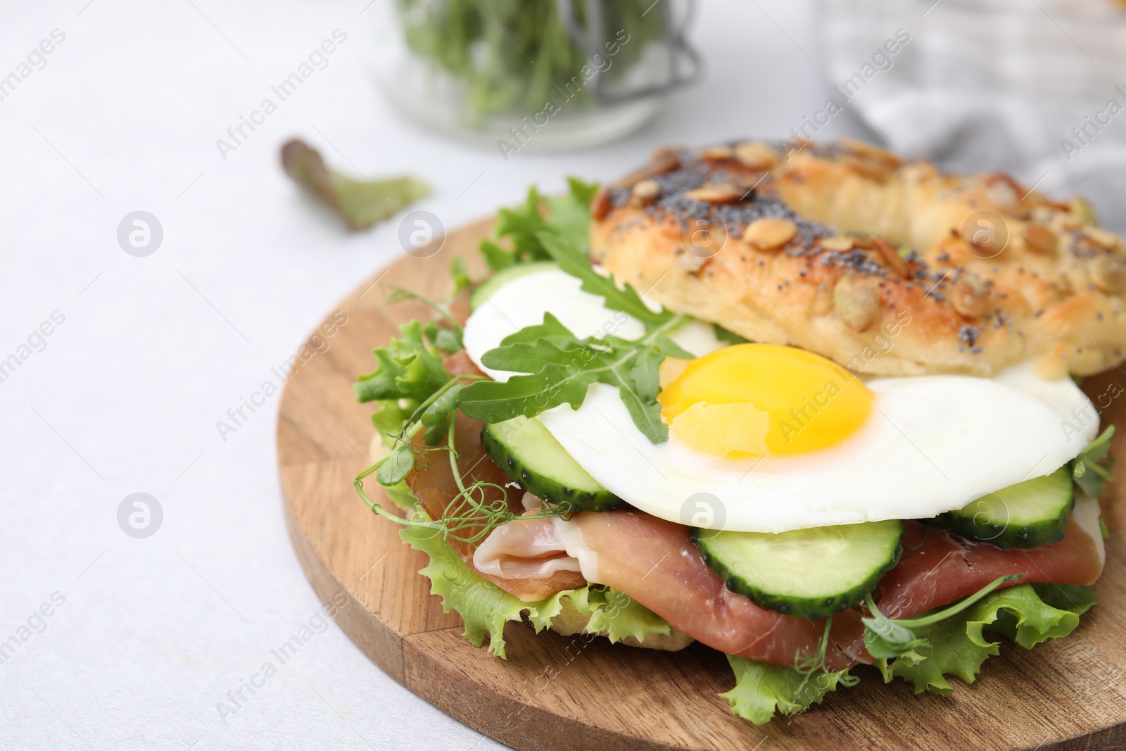 Photo of Tasty bagel with cured ham, egg, cucumber and salad mix on light table, closeup. Space for text