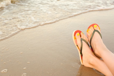 Photo of Closeup of woman with stylish flip flops on sand near sea, space for text. Beach accessories