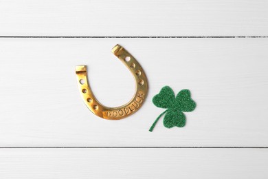 Photo of St. Patrick's day. Golden horseshoe and green decorative clover leaf on white wooden table, flat lay
