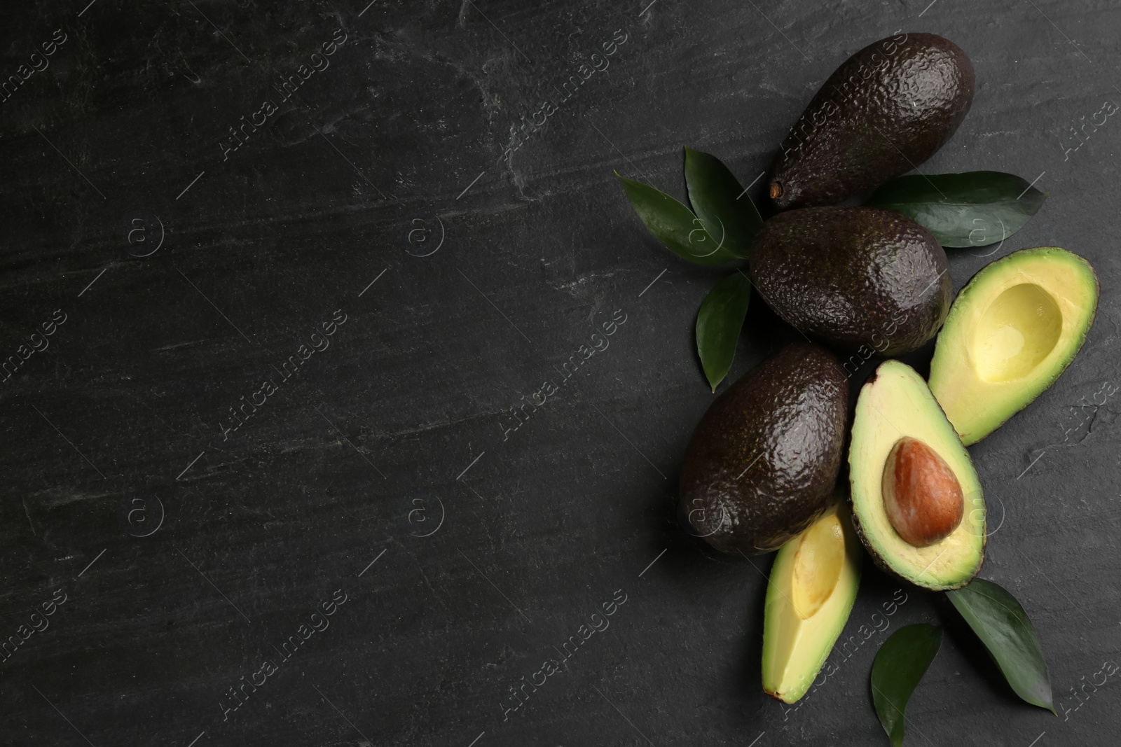 Photo of Whole and cut avocados with green leaves on black table, flat lay. Space for text