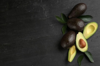 Photo of Whole and cut avocados with green leaves on black table, flat lay. Space for text