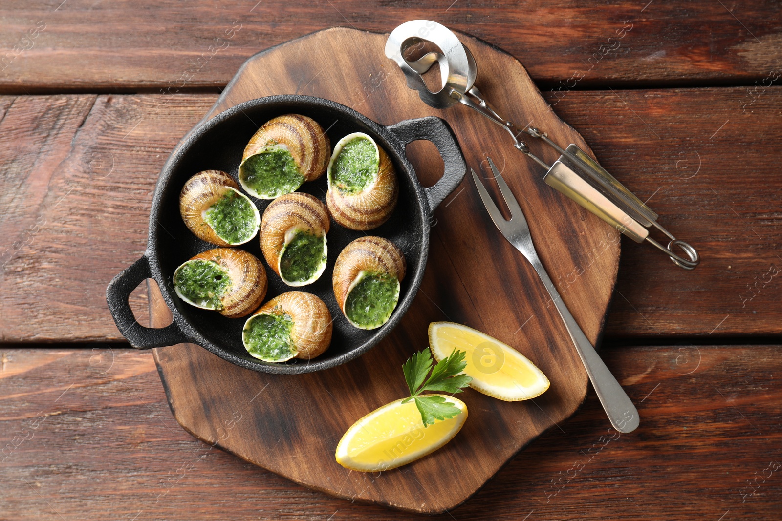 Photo of Delicious cooked snails in baking dish served on wooden table, flat lay