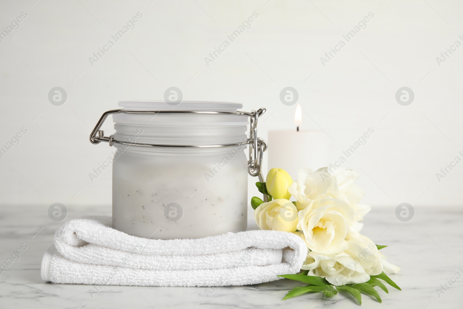 Photo of Jar of salt scrub, freesia flowers and towel on white marble table