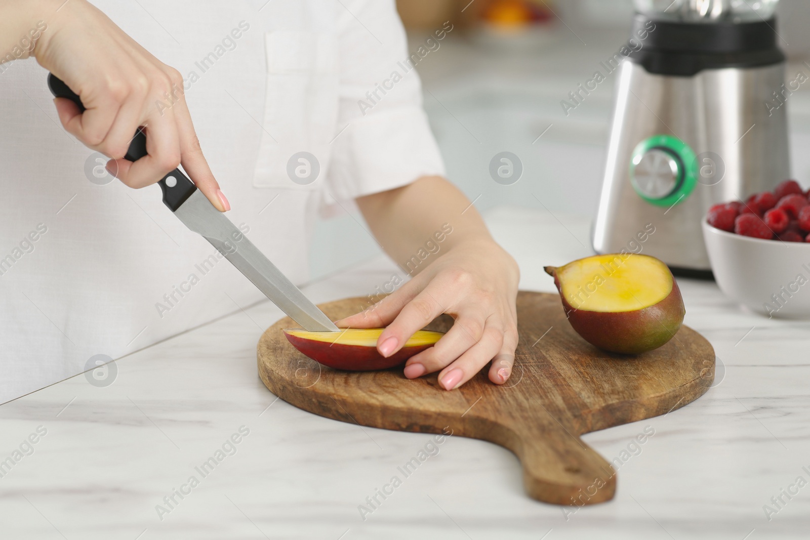 Photo of Woman preparing mango for tasty smoothie at white marble table in kitchen, closeup