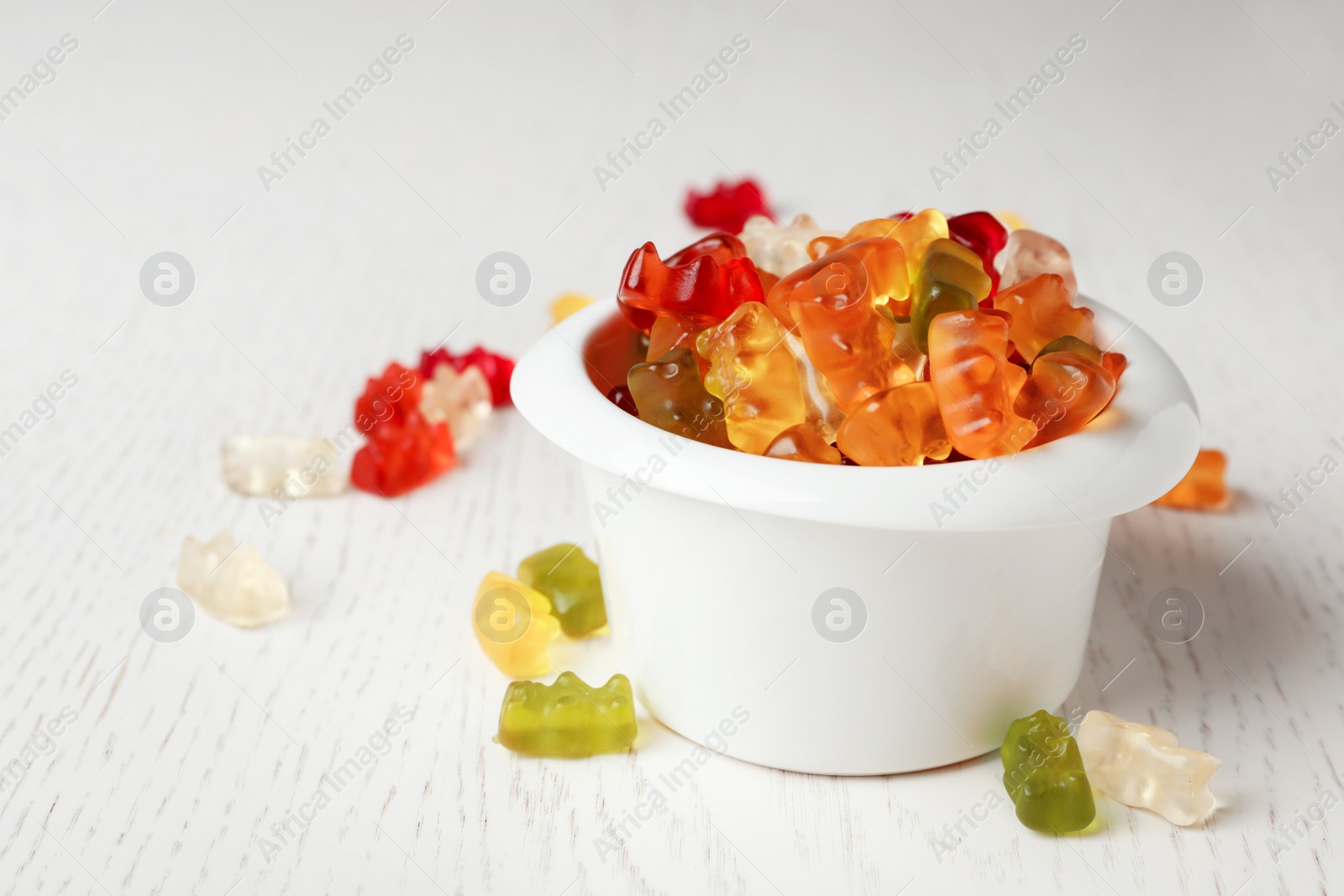 Photo of Bowl with delicious jelly bears on light wooden table. Space for text