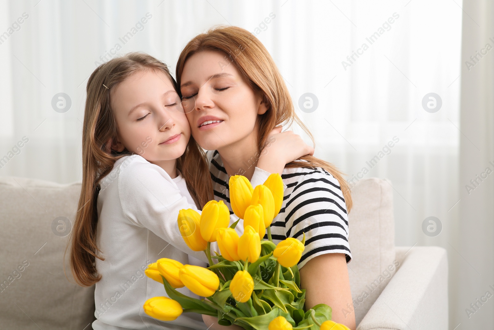 Photo of Mother and her cute daughter with bouquet of yellow tulips on sofa at home