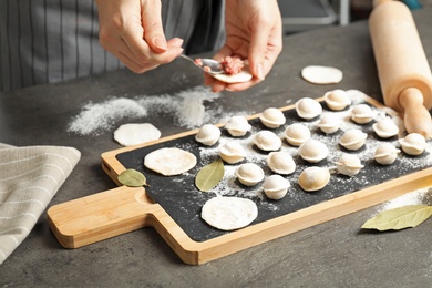 Photo of Woman cooking delicious dumplings over grey table, closeup