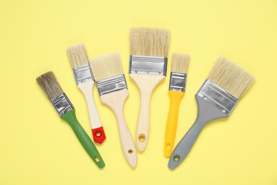 Photo of Many different paint brushes on pale yellow background, flat lay