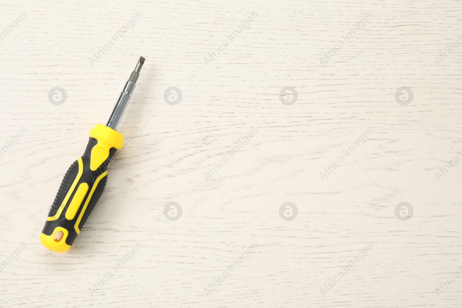 Photo of Screwdriver with yellow handle on white wooden table, top view. Space for text